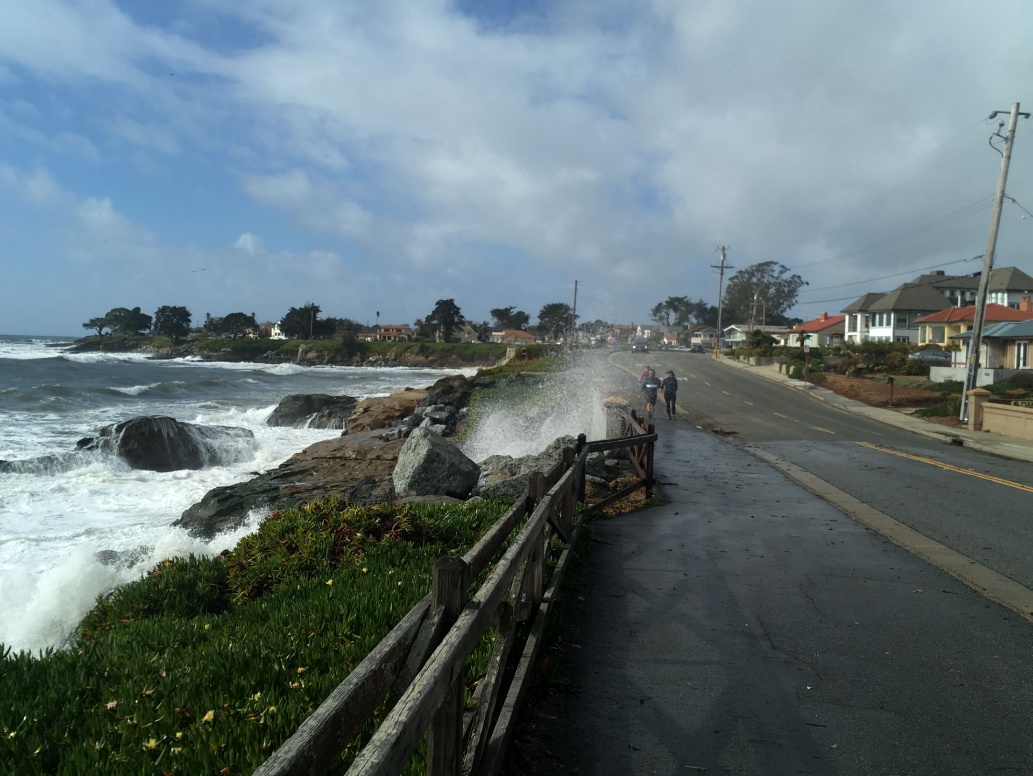Coastal flooding along a California road with waves crashing over rocks during a storm